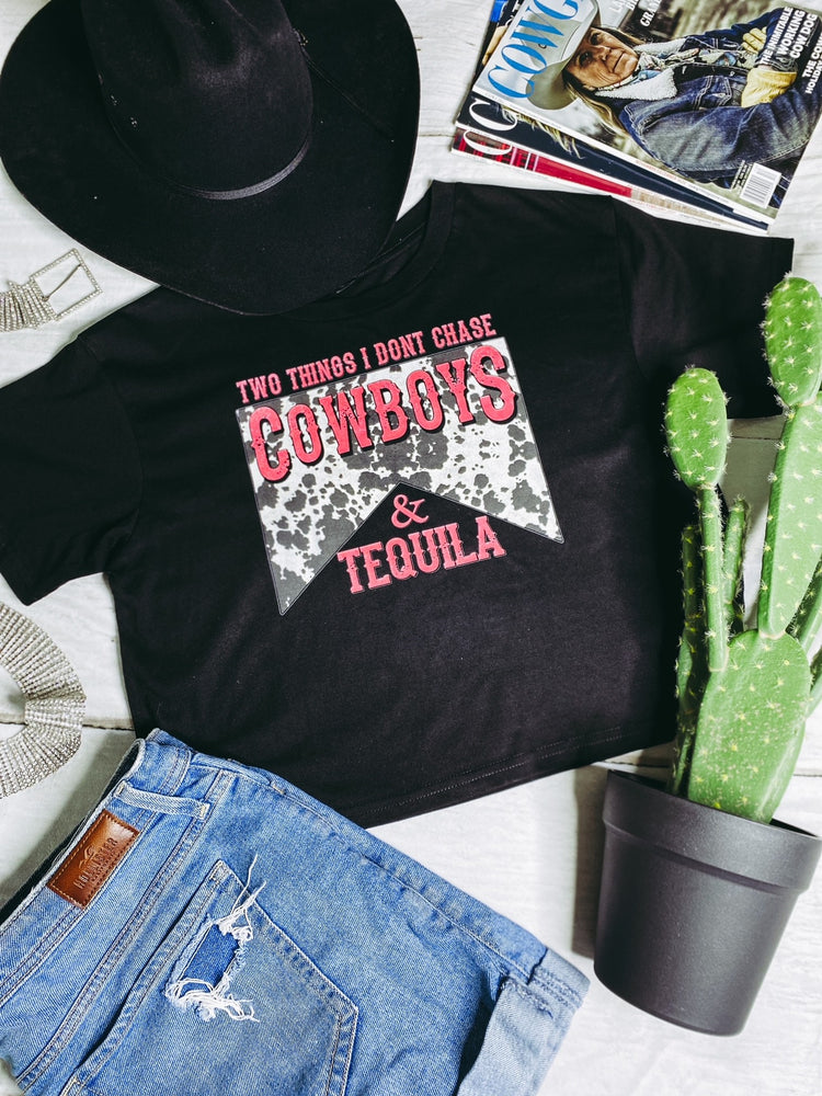 Flatlay showing a black crop top with a printed graphic saying Two Things I Don't Chase Cowboys & Tequila